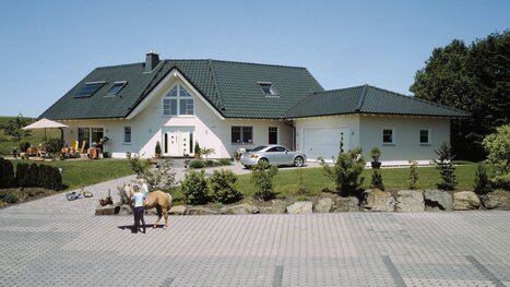 Fingerhut Einfamilienhaus grünes Dach hell verputzt Gaube über Eingangsbereich Doppelgarage Terrasse 