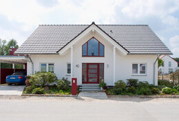 Fingerhut Einfamilienhaus dunkles Satteldach weißer Putz Gaube Eingangsbereich rote Haustür roter Standbriefkasten Carport 