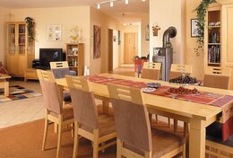 Wohn-Esszimmer Holz Couchtisch Holz Eckschrank Esszimmertisch mit 6 Stühlen mit braunem Stoff rote Tischdecke heller Fliesenboden Kamin 
