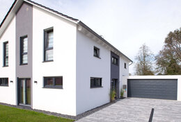 Fingerhut Einfamilienhaus schwarzes Satteldach weiß verputzt mit grau abgesetzten Teilflächen Doppelgarage mit grauem Garagentor